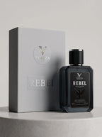 A dark glass bottle of VORZA Rebel cologne stands in front of its light gray packaging box on a round pedestal against a neutral gray background.